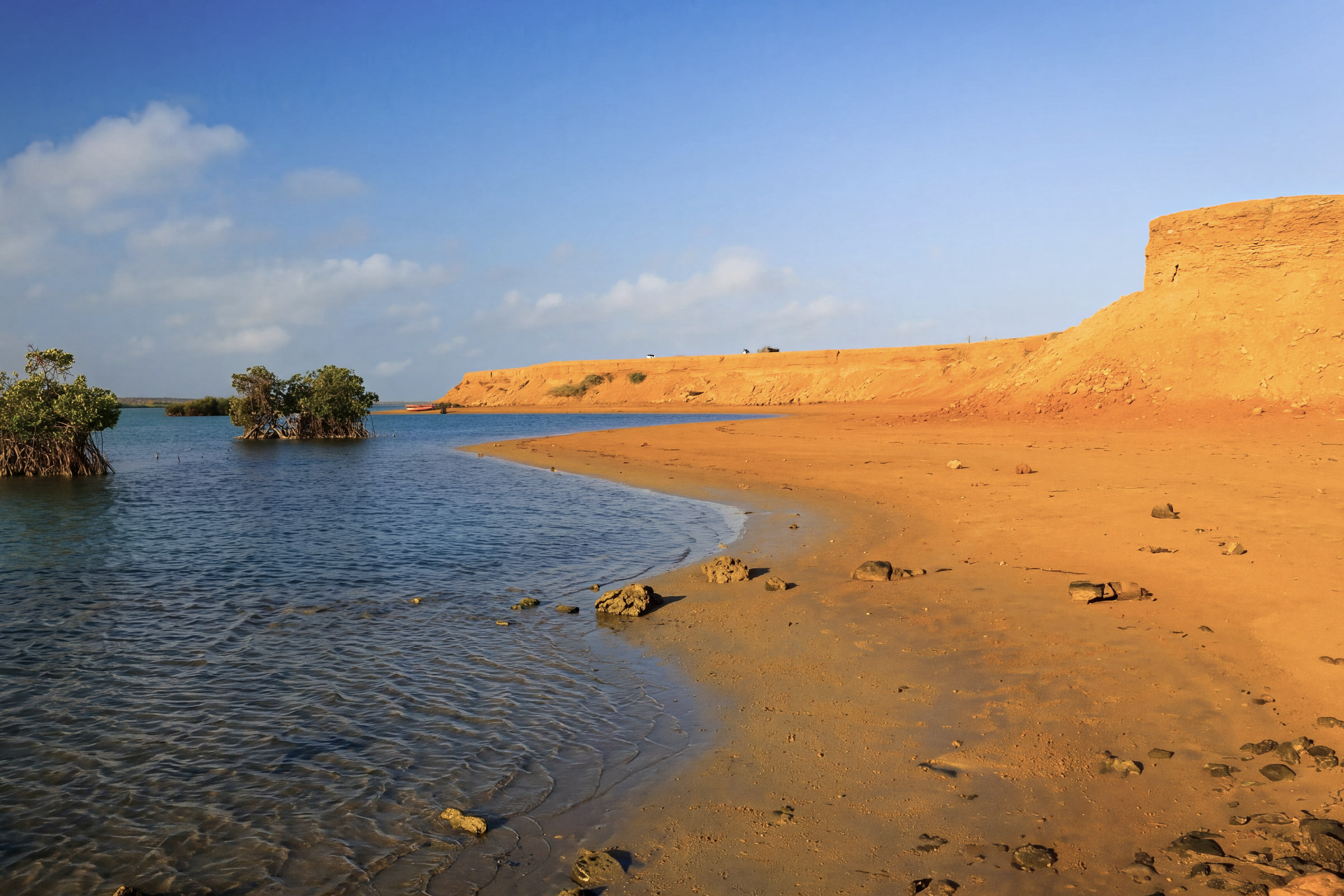 Barrancos de tierra ocre que bajan a la orilla de Bahía Hondita, con dos manglares aislados en el agua, en la Alta Guajira.
