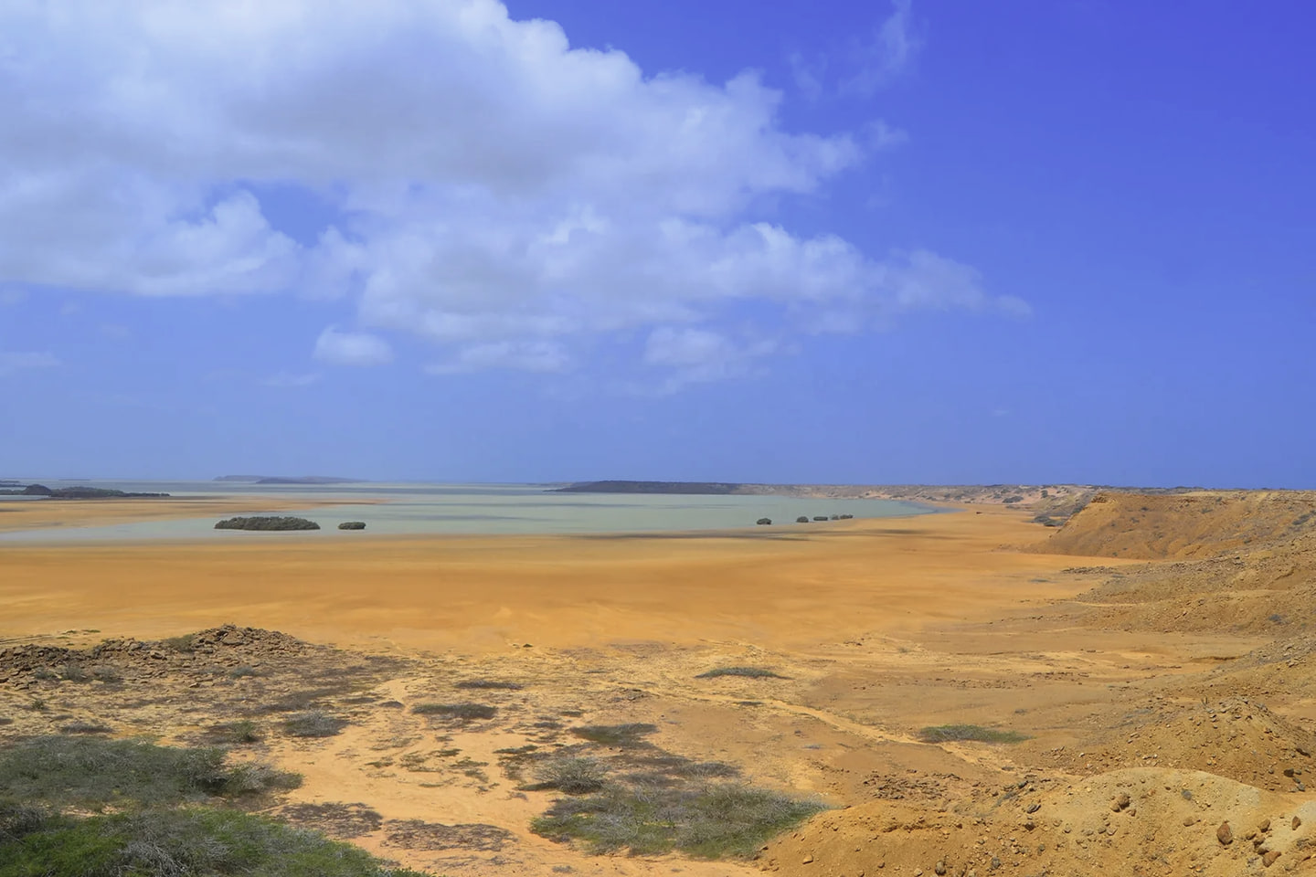 Llanura de arena y matorral bajo que llega hasta el mar en la zona de Punta Gallinas, con cielo azul y nubes.
