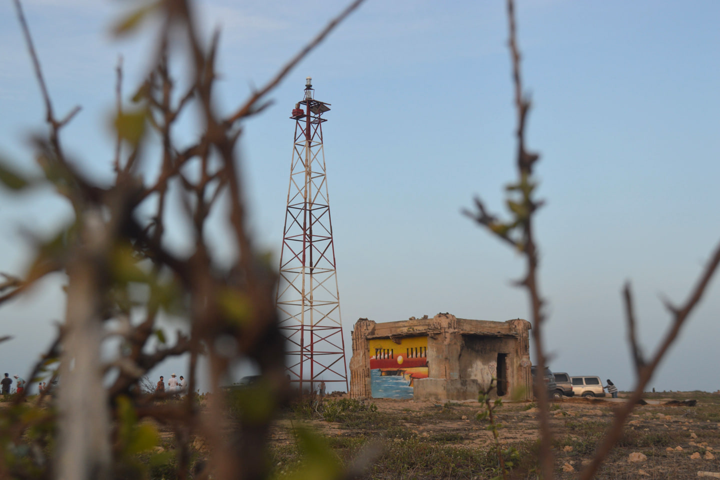 The metal tower of the Punta Gallinas lighthouse and the painted hut beside it, seen through dry branches in the foreground.