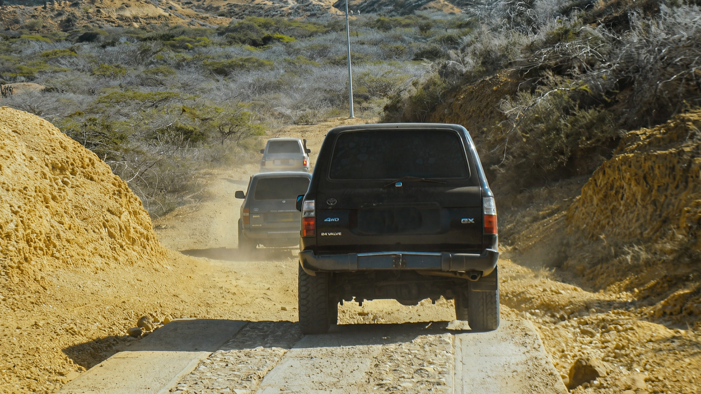 Three 4×4 vehicles in a line on a dirt track through dry scrub in Alta Guajira, on the tour route.