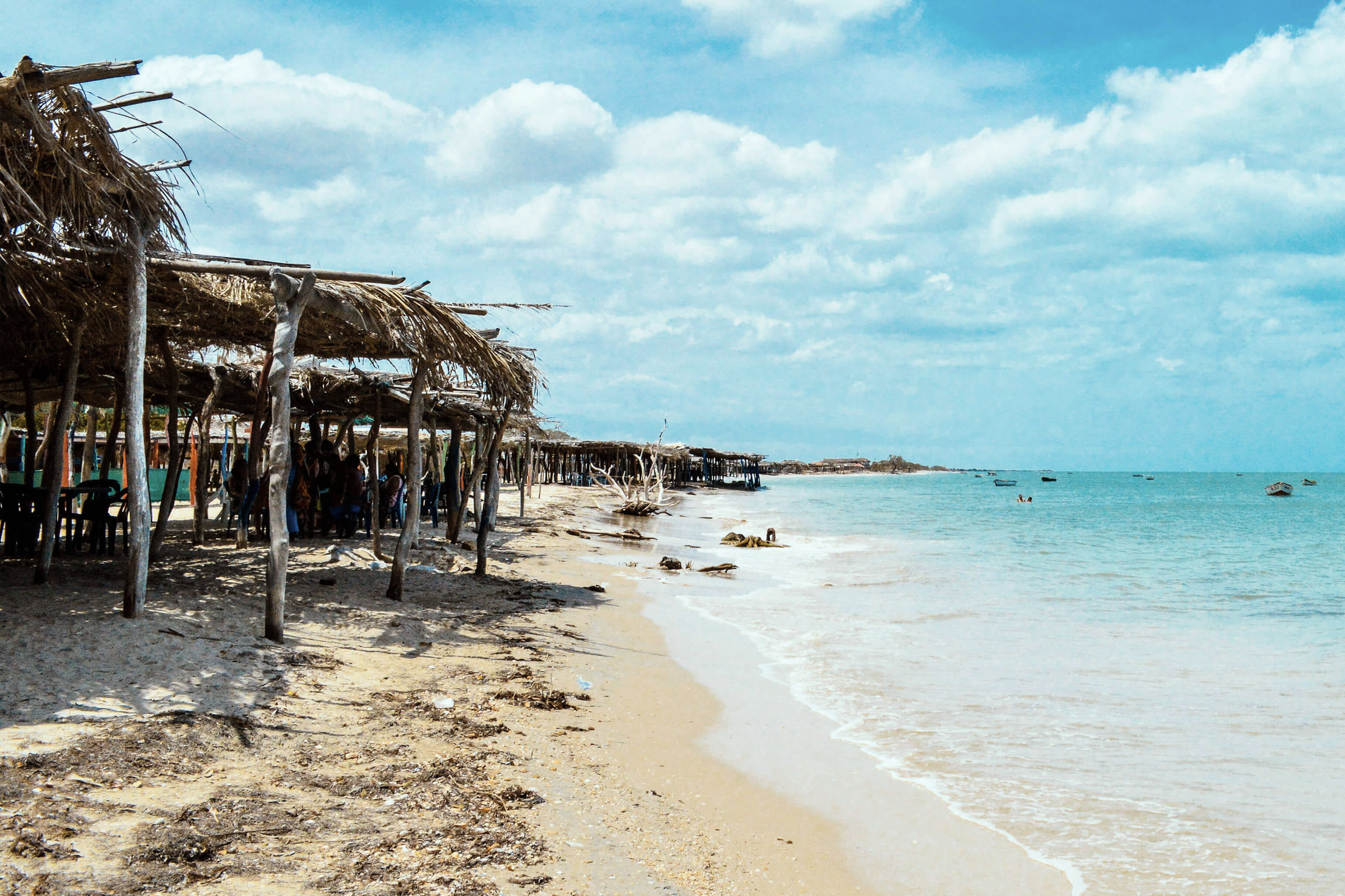 Ranchos de palma sobre la arena de la playa de Mayapo, con el mar en calma a la derecha.