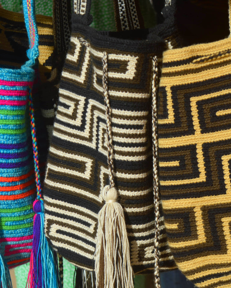 Mochilas wayuu tejidas a mano colgadas en exhibición, con dibujos geométricos en negro, crema y colores vivos.