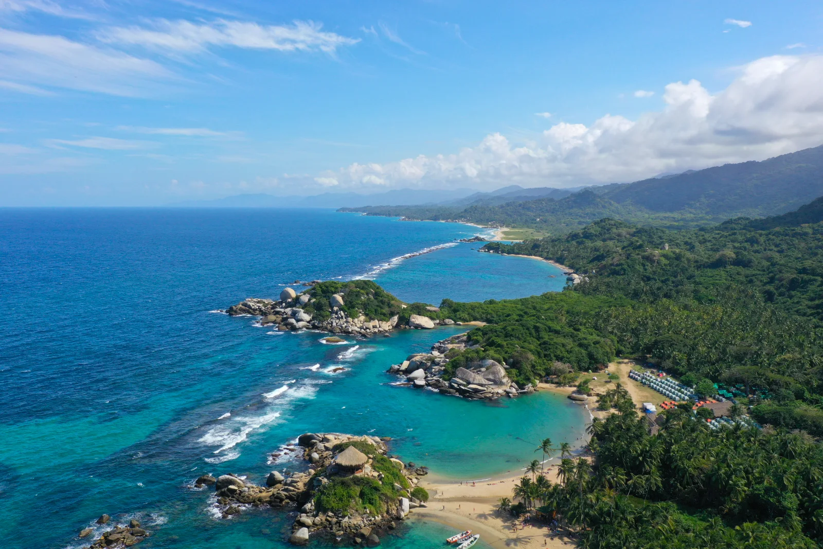 Vista aérea de la costa del Parque Tayrona con el Cabo San Juan del Guía en primer plano, bahías turquesa, playas largas y montañas.