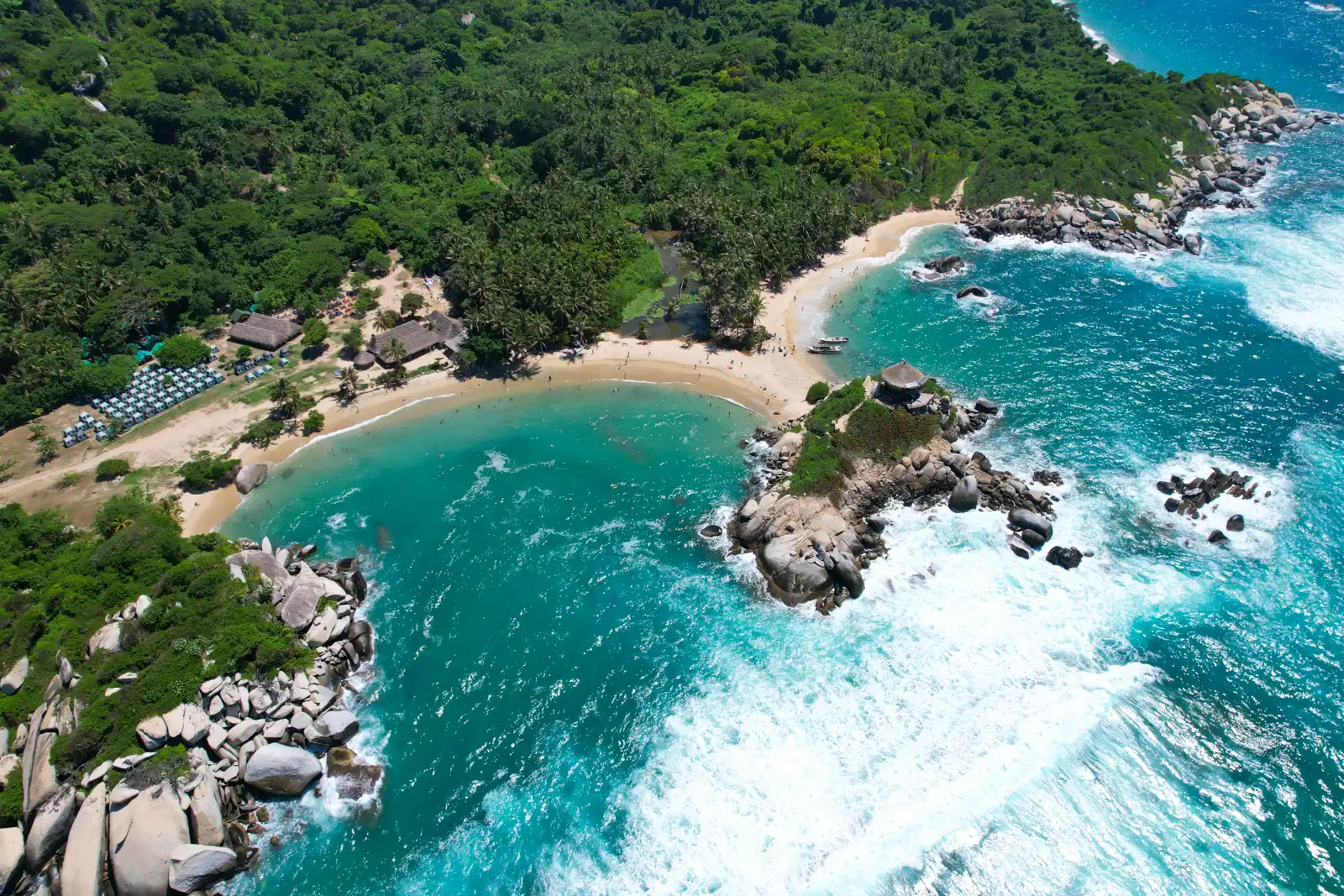 Vista aérea del Cabo San Juan del Guía con dos ensenadas de agua turquesa, el islote con el kiosco, la zona de carpas y el oleaje.
