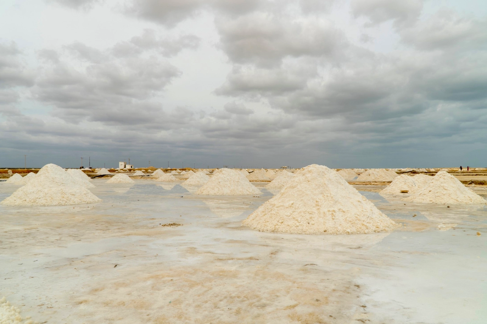 Monticules de sel blanc dans les salines de Manaure, sur des bassins peu profonds et sous un ciel couvert à la lumière plate.