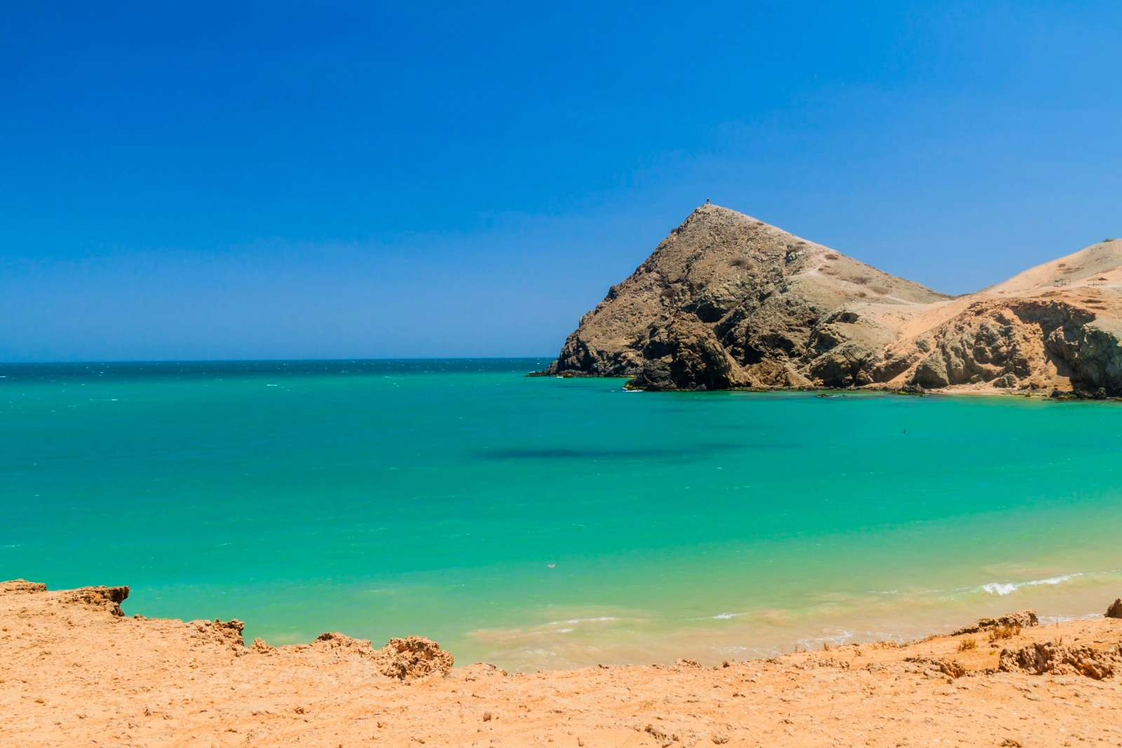 Le Pilón de Azúcar, colline rocheuse au-dessus d'une eau turquoise, vu depuis un bord de sable et de roche, à Cabo de la Vela.