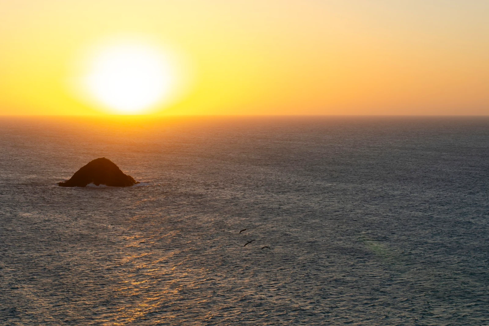 Soleil bas sur la mer avec un îlot rocheux en silhouette et des reflets dorés sur l'eau, en fin de journée sur la côte de La Guajira.